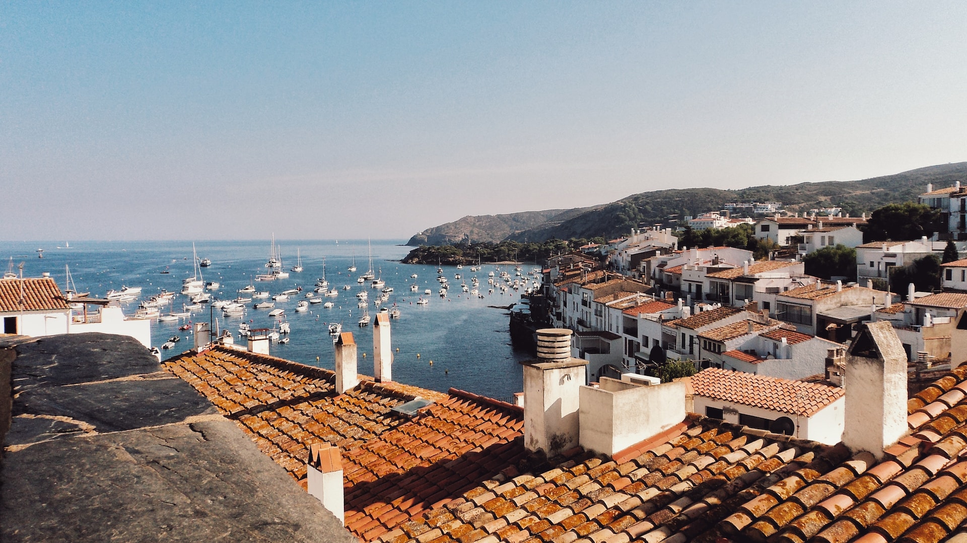 Terracotta rooftops overlooking a bay with sailboats in a coastal town