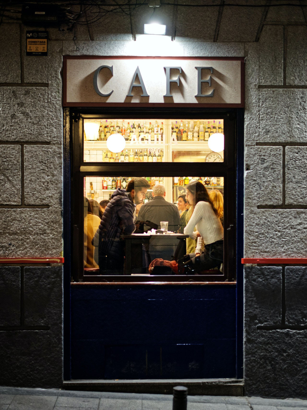 Lit café window at night with people sitting at a table inside