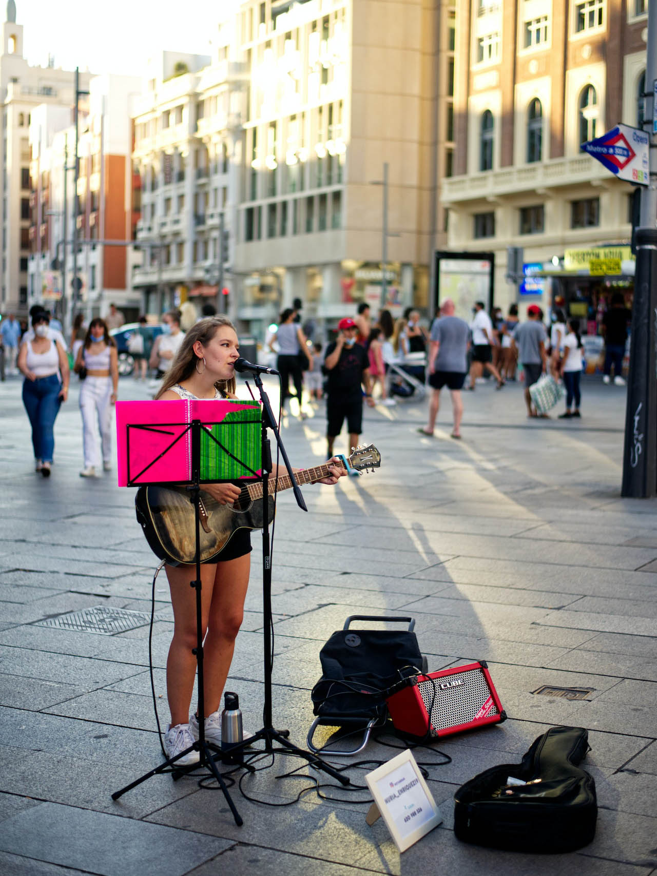 Young woman singing and playing guitar on a pedestrian street with an amplifier