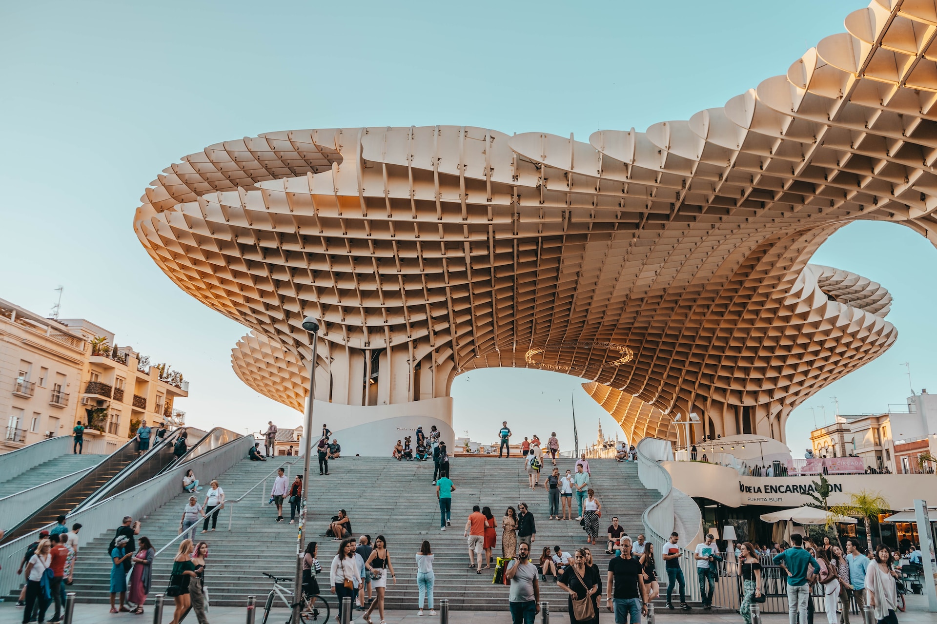 Large wooden lattice canopy structure above a busy stepped plaza