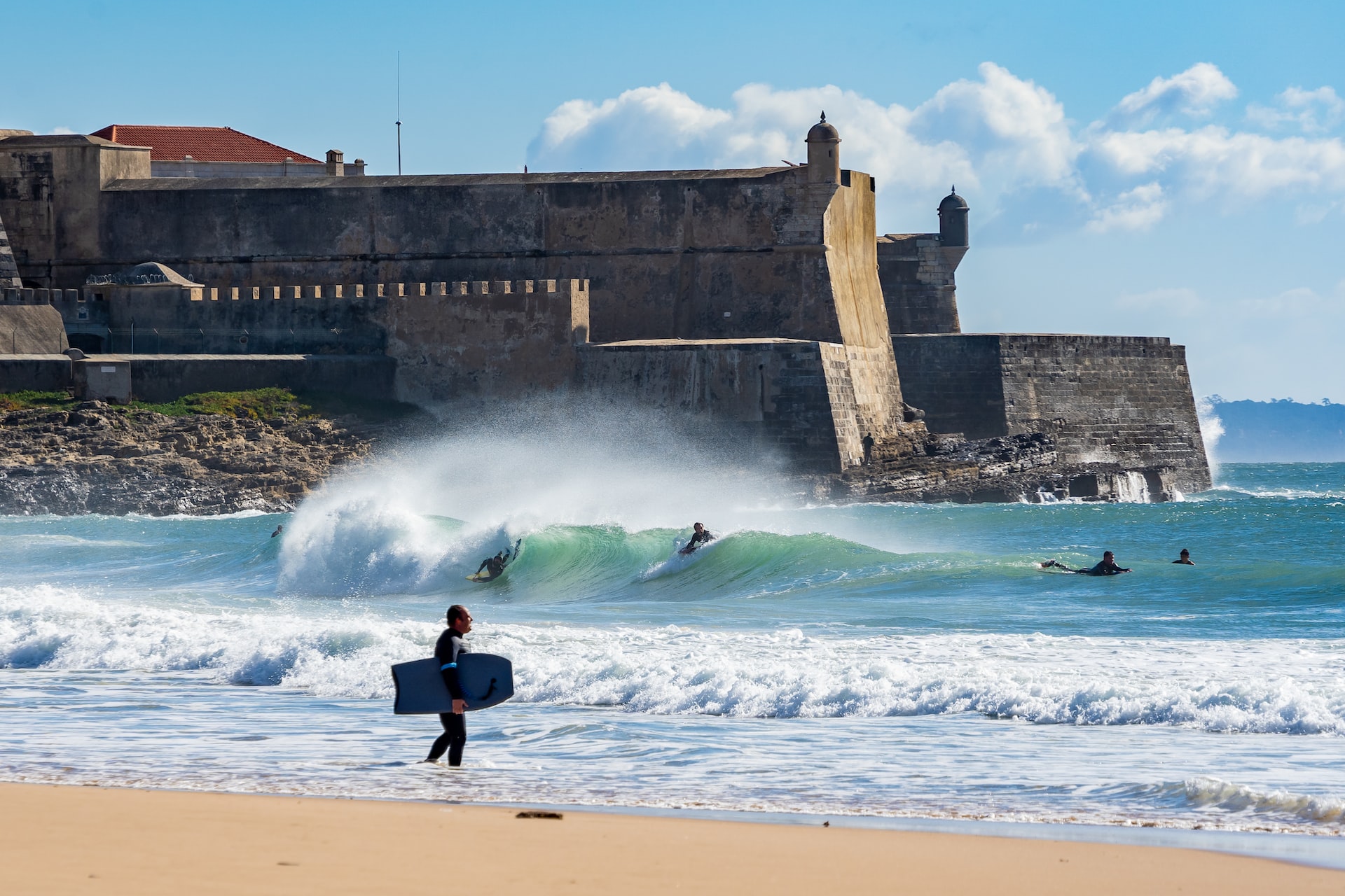 Surfers in the waves below an old stone fortress