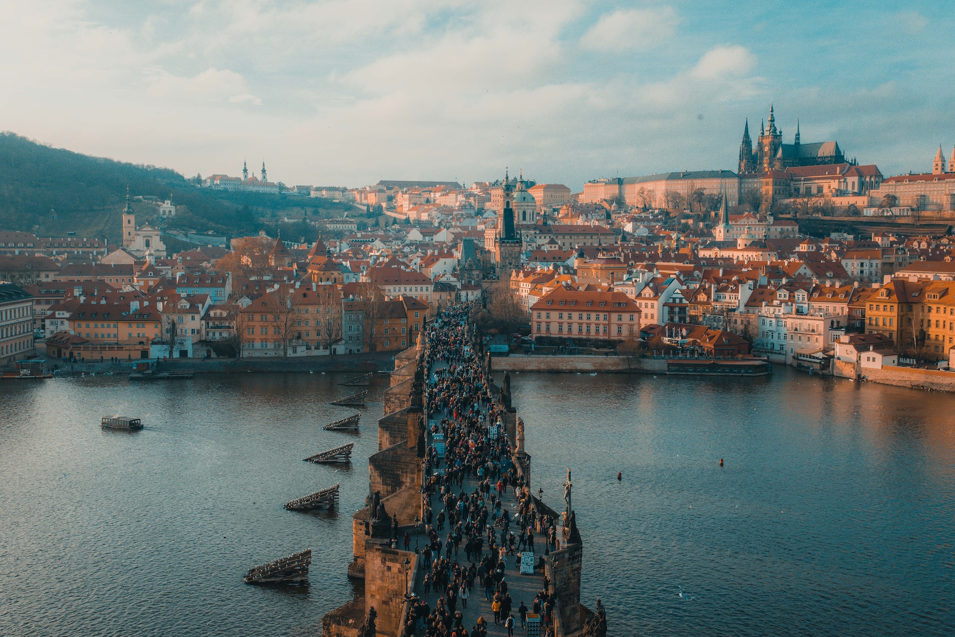 Crowded stone bridge over a river with a historic hillside city at sunset
